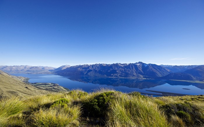 Mountain range reflected in a calm lake with grassy foreground