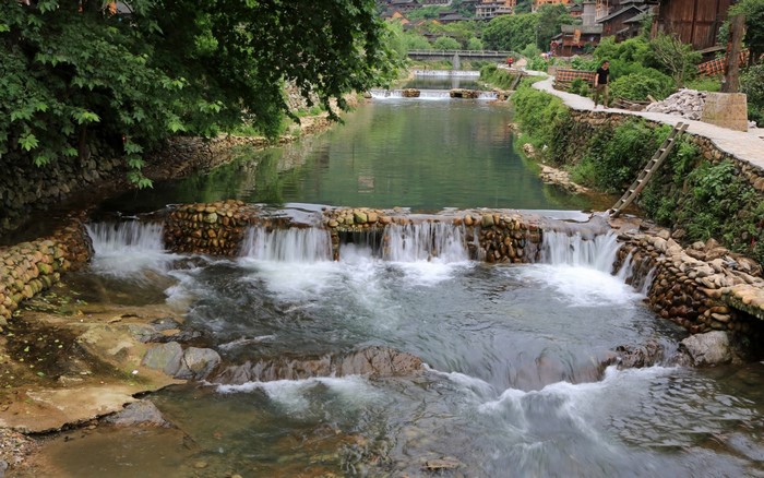 River with small waterfalls and stone banks in a village