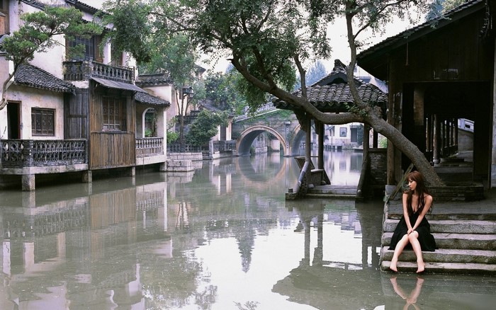 Woman in black dress sitting on steps by a canal