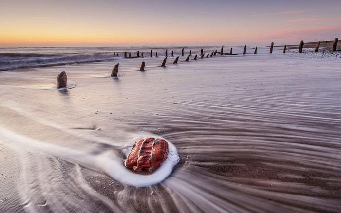 Beach with wooden posts and a rock at sunset