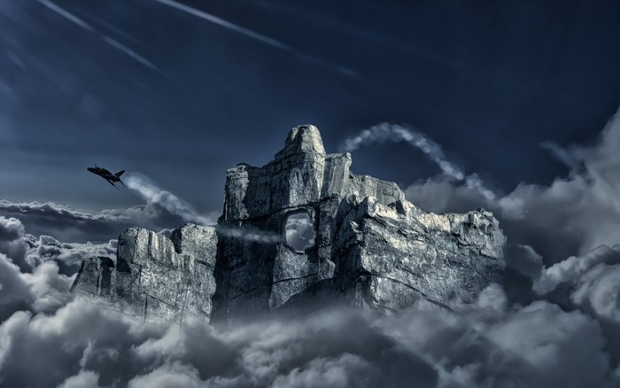 Jet fighter flying near a rocky mountain peak through clouds