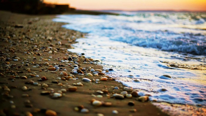 Pebbles on a beach at sunset with waves