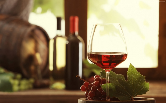 Wine glass with red wine, bottles, grapes, and barrel