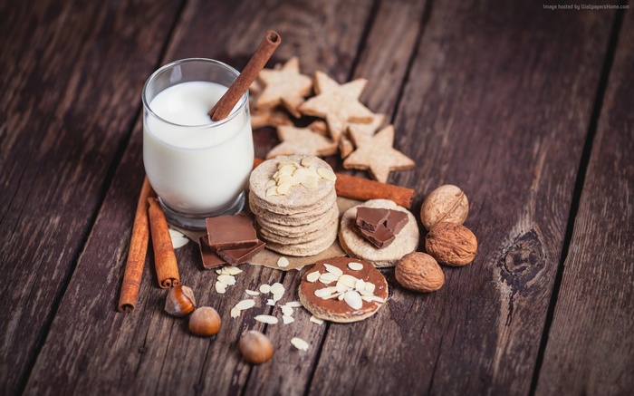 Milk, cookies, chocolate, nuts, and cinnamon sticks on wooden table