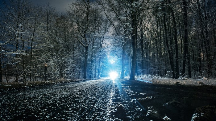 Bright headlights on a snowy forest road at night