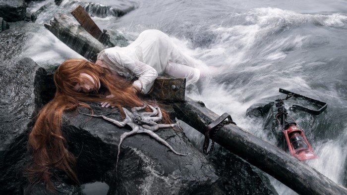 Woman with red hair and octopus on rocks in water