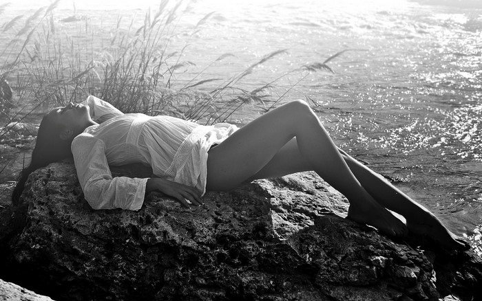 Woman Lying on Rock by Sunlit Water in Monochrome