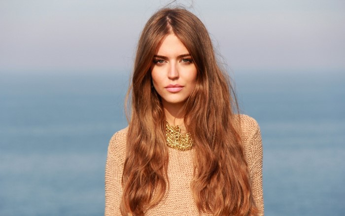 Woman with long brown hair wearing a beige sweater and gold necklace