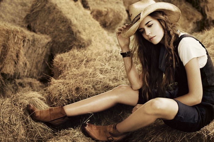 Woman in cowboy hat sitting in hay bales