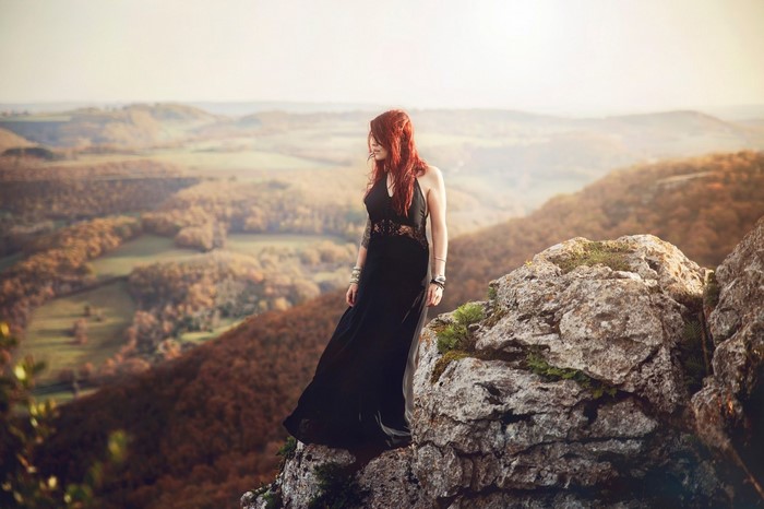 Woman in black dress on a rocky cliff overlooking a valley