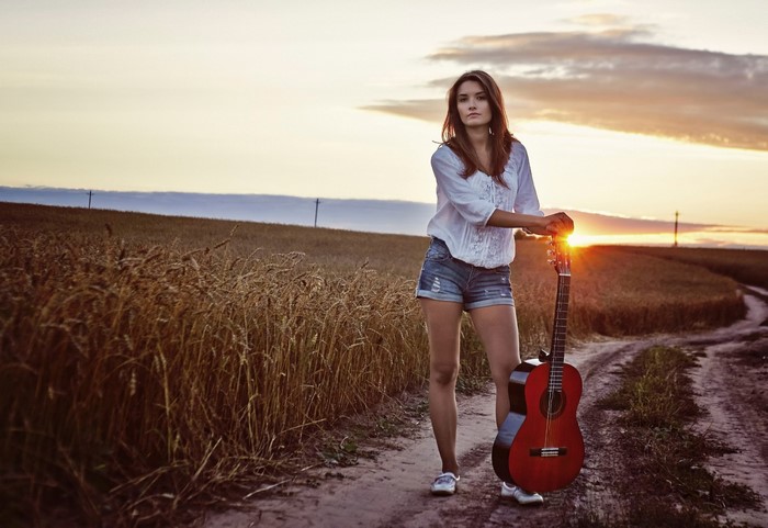 Woman with guitar in a wheat field at sunset