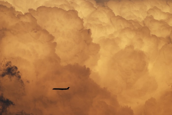 Airplane flying through dramatic sunset clouds