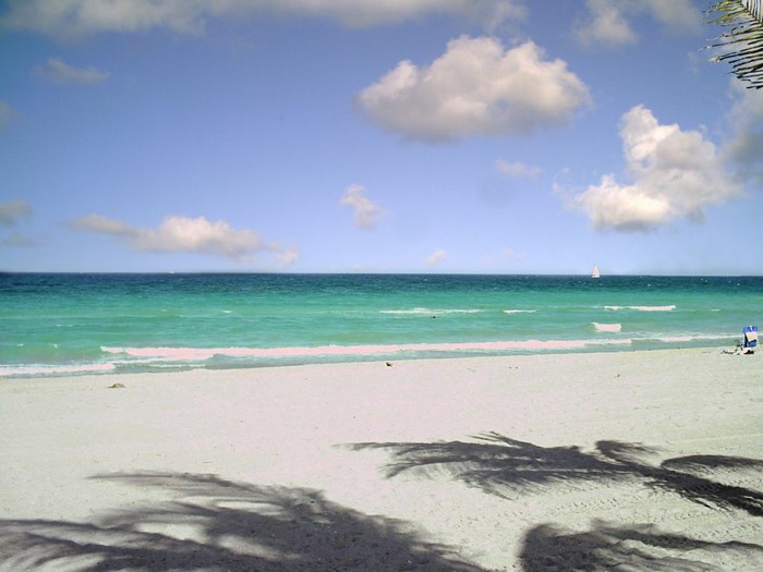 Beach with ocean, clouds, and sailboat
