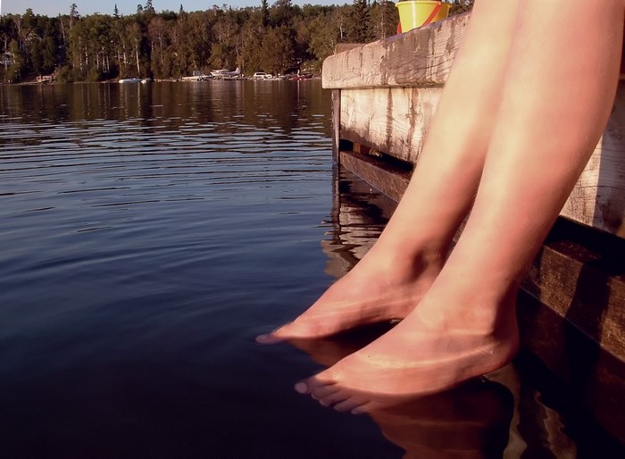 Person's feet dangling in lake water from a wooden dock