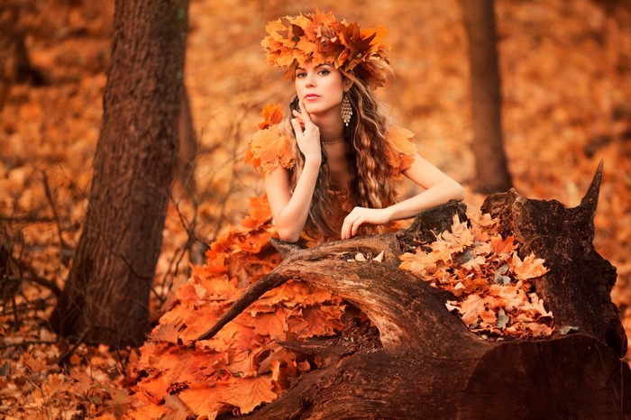 Woman in a dress made of autumn leaves in a forest