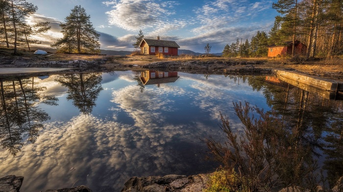 Red cabin reflected in a calm lake with trees and sky