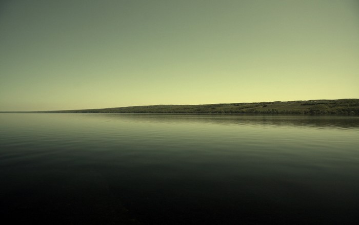 Calm lake with distant tree-covered hills under a pale sky