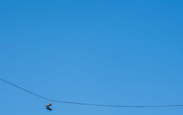 Pair of shoes hanging on a wire against a clear blue sky