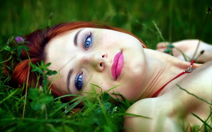 Woman with red hair and blue eyes lying in grass