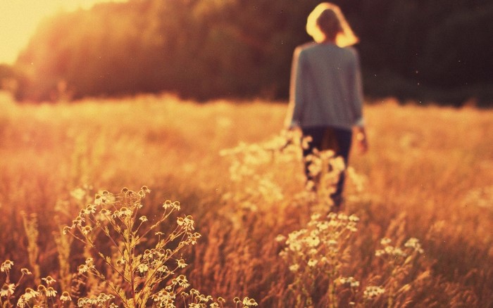 Woman walking through a sunlit field of flowers