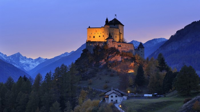 Illuminated castle on a hill in the Alps at dusk