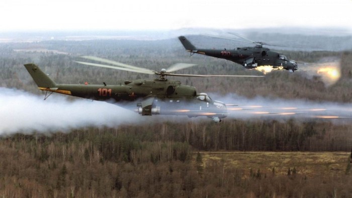 Two Mi-24 helicopters firing weapons over a forest