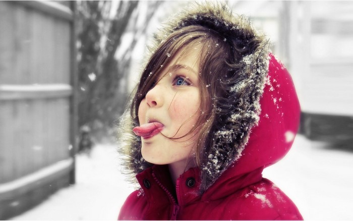 Girl in red hooded coat sticking tongue out in snow