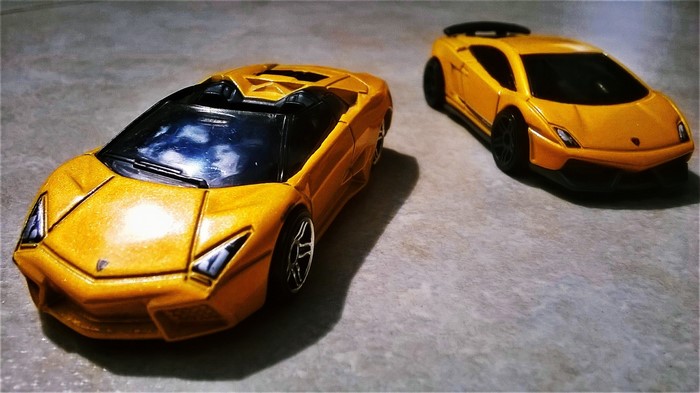 Two yellow Lamborghini toy cars on a textured surface