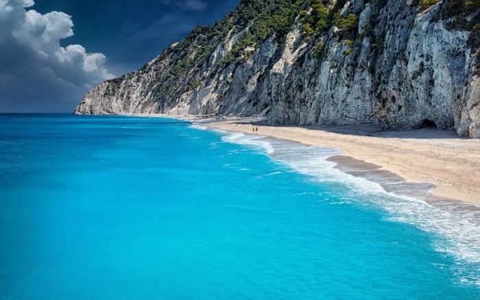 Turquoise sea meets a sandy beach and a rocky cliffside