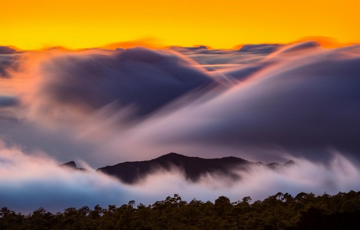 Mountain peaks emerge from clouds at sunrise with orange sky