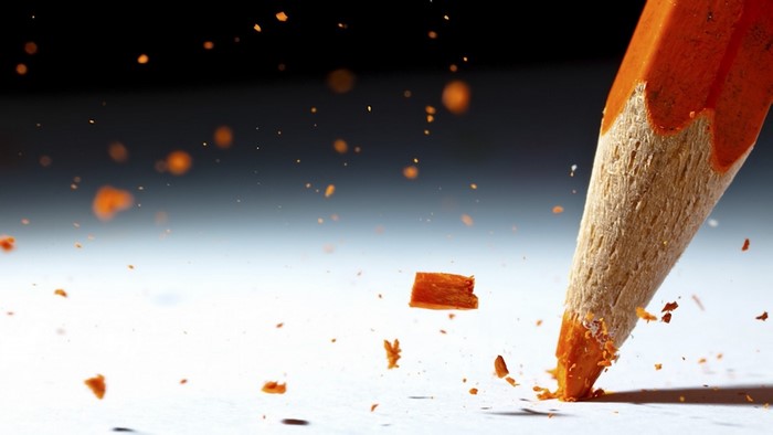 Close-up of orange pencil breaking on white surface