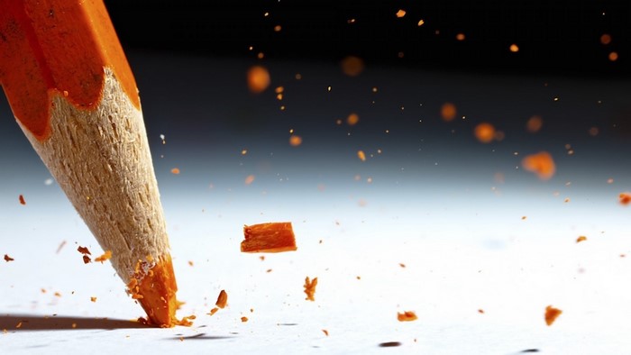 Close-up of an orange pencil breaking, scattering shavings