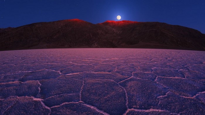 Moonlit desert landscape with cracked ground and mountains