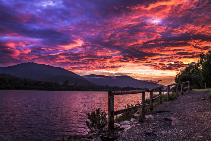 Dramatic sunset over a lake with mountains and a wooden fence
