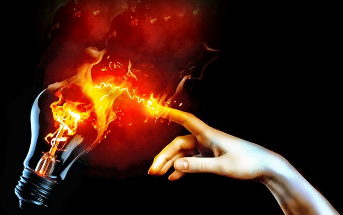 Hand touching a burning lightbulb with fire and electricity