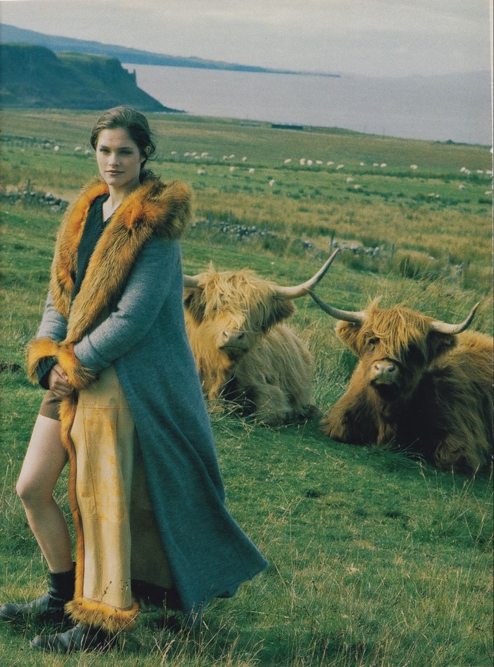 Woman in fur-trimmed coat with Highland cows in a field
