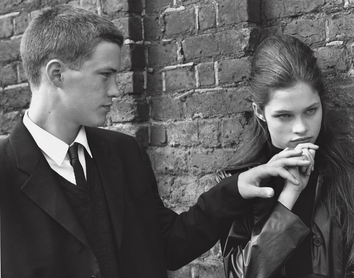 Man in suit touches woman's hand by brick wall