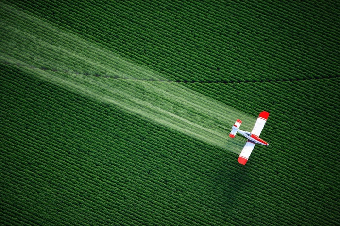 Airplane spraying a green field from above