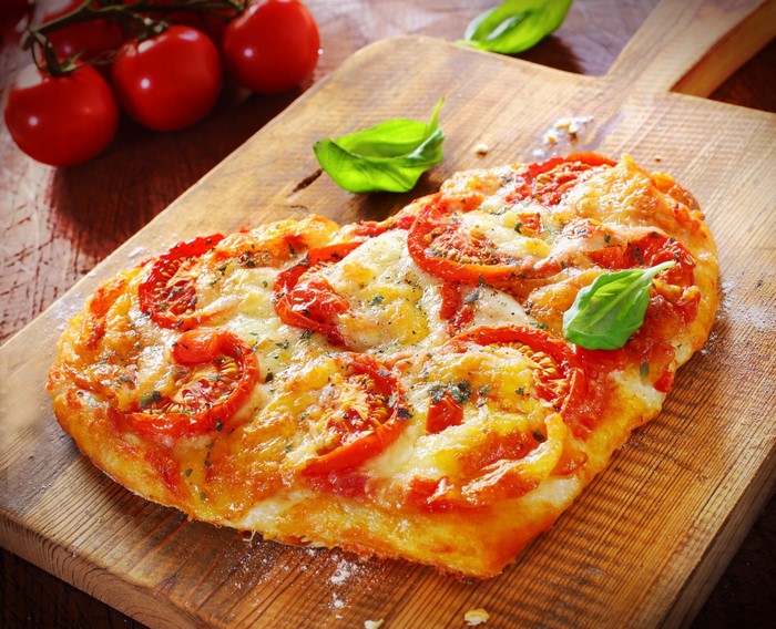 Heart-shaped pizza with tomatoes and basil on a wooden board