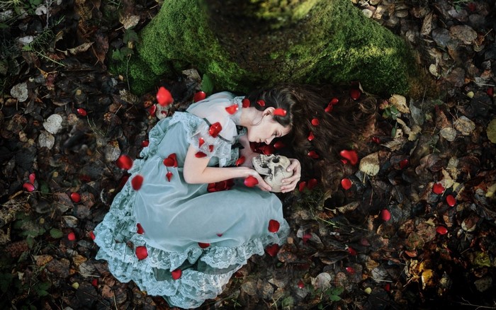 Woman in a dress holding a skull surrounded by rose petals