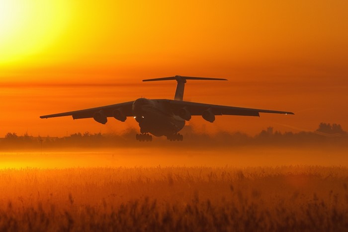 IL-76 aircraft taking off at sunset over a field