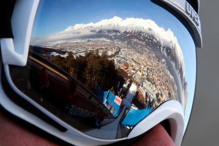 Ski goggles reflecting a snowy mountain town and ski jump