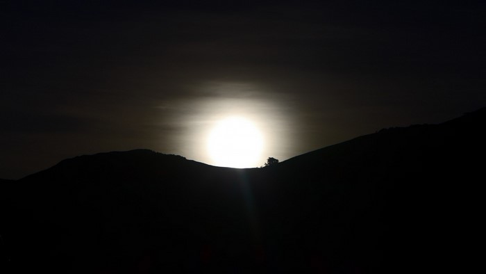 Full moon setting behind silhouetted mountains