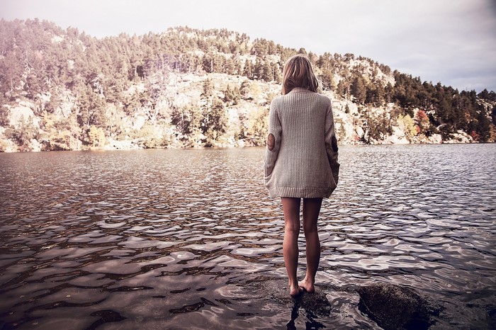 Woman in sweater standing in lake with mountain background
