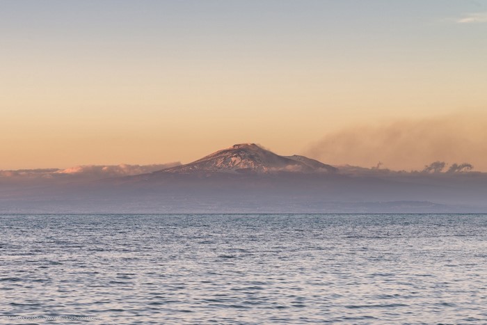 Volcano erupting smoke over the sea at sunset