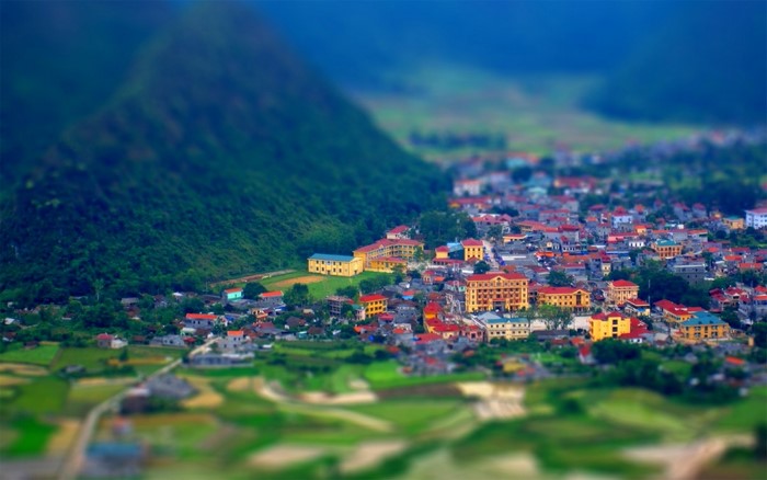 Tilt Shift Aerial View of a Town Nestled Beside a Lush Green Hill