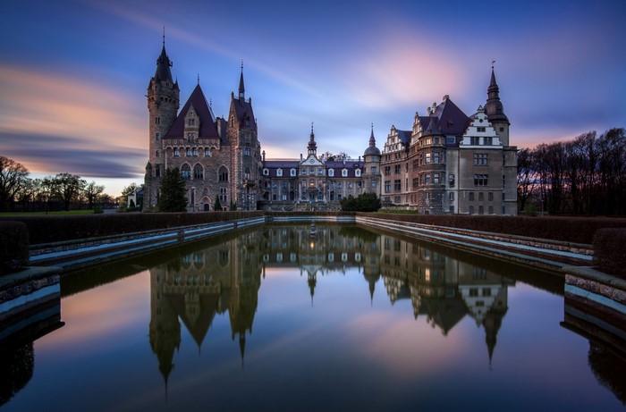Moszna Castle reflected in water at dusk