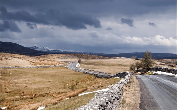 Winding road through a rural landscape with snow-capped mountains