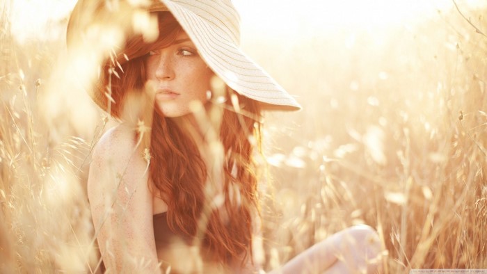Redhead woman with freckles wearing a hat in a field
