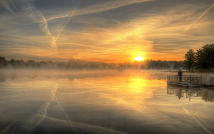 Sunrise over a misty lake with a person on a pier